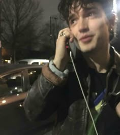 a young man talking on a cell phone while standing in front of a parked car