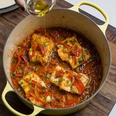 a pan filled with chicken and vegetables on top of a wooden table next to a glass of wine