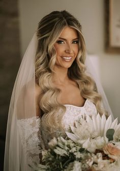 a woman in a wedding dress holding a bridal bouquet and smiling at the camera