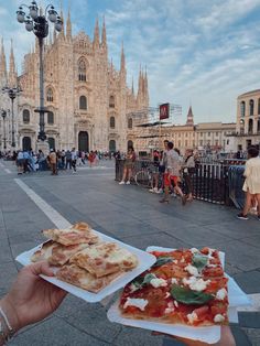 a person holding two slices of pizza in front of a cathedral