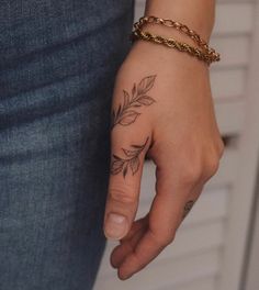 a woman's hand with a small leaf tattoo on her left wrist and a gold chain bracelet