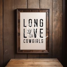 a wooden table sitting in front of a wall with a framed poster on it that says long love cowgirls