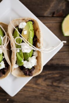 two tacos with toppings are sitting on a napkin next to lime wedges