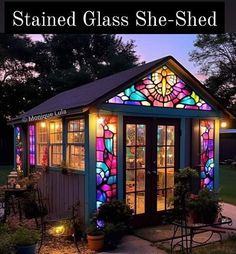 a small building with stained glass windows and lights on it's sides in the evening