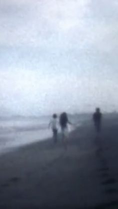 three people are walking along the beach on a foggy day