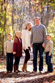 a family posing for a photo in the woods with leaves on the ground and trees behind them