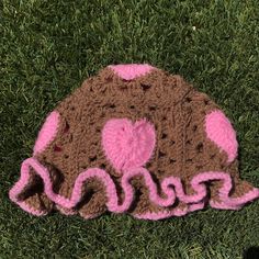 a crocheted hat with pink and brown hearts on the front sitting in grass