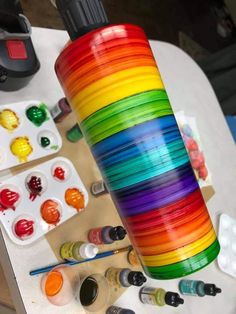 a rainbow colored vase sitting on top of a table filled with paints and brushes next to other items