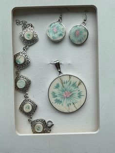 an assortment of jewelry is displayed in a white box with silver accents and flowers on it