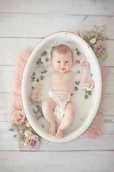 a baby in a bathtub surrounded by flowers and greenery on a white wooden floor