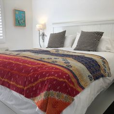 a bed with pillows and blankets on top of it next to a wall mounted lamp