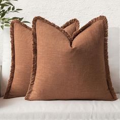 two brown pillows sitting on top of a white couch next to a potted plant