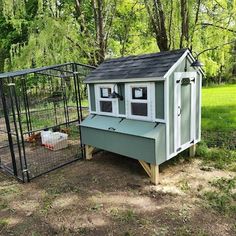 a chicken coop in the middle of a grassy area with trees and grass behind it