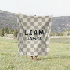 a person standing in the grass holding up a checkered blanket that says, llam james