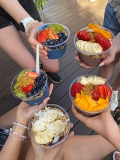 four people holding up bowls of fruit and yogurt