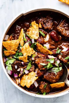 a bowl filled with chili beef and tortilla chips on top of a table