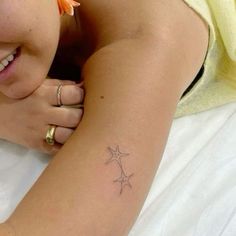 a woman laying on top of a bed with a star tattoo on her left arm