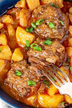 a blue bowl filled with meat, potatoes and gravy next to a fork