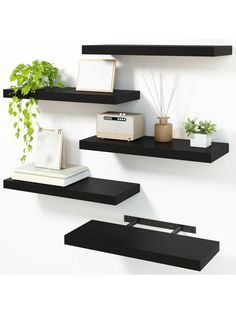 three black floating shelves with plants and pictures on them, one shelf has a plant in it