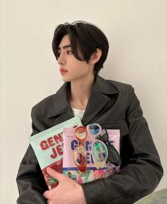 a young man is holding a book in his hands and looking at the camera while wearing a leather jacket