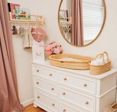 a white dresser topped with a baby crib next to a mirror