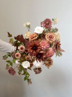 a person holding a bouquet of flowers in their hand with white and pink blooms on it