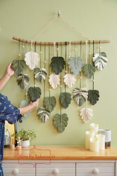 a woman is placing leaves on a wall hanging from a wooden frame over a dresser