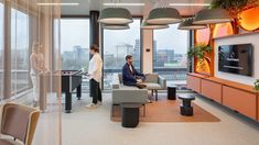 two people are sitting in a living room with large windows looking out onto the city