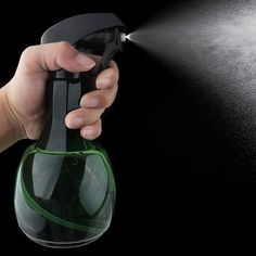 a hand holding a sprayer spraying water onto a green glass bottle with black background