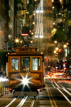 a trolley car traveling down a city street at night with light streaks on it's side