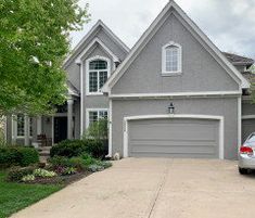 a car is parked in front of a large gray house with white trim and windows