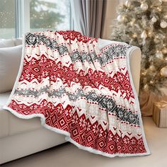 a red and white blanket sitting on top of a couch next to a christmas tree