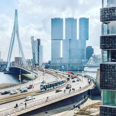 cars are driving on the road in front of tall buildings and a bridge over water