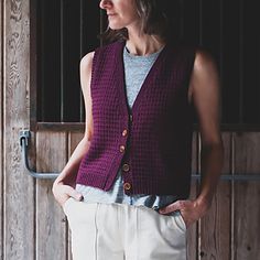 a woman standing in front of a wooden wall wearing a purple sweater and white pants