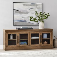 a wooden entertainment center with glass doors and shelves on the bottom, in front of a painting