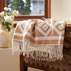 a brown and white blanket sitting on top of a wooden bench next to a vase with flowers