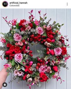 a hand holding a wreath with pink and red flowers