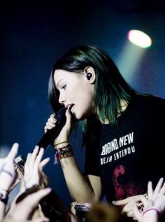 a woman holding a microphone up to her ear while standing in front of a crowd