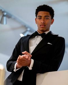 a young man in a tuxedo poses for the camera with his hands clasped