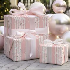 three wrapped presents sitting on the ground with pink and white ornaments in the background,