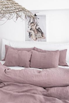 a bed with pink sheets and pillows in a bedroom next to a painting on the wall