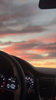 the dashboard of a car with an orange sky in the background and clouds above it