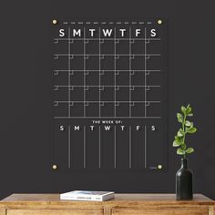 a black and white calendar on a wall next to a vase with a plant in it