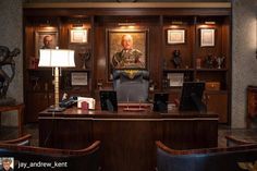 an office with two desks, chairs and pictures on the wall above them in wood paneling