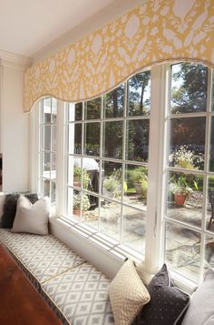 a window seat in front of a bay window with yellow and white drapes on it