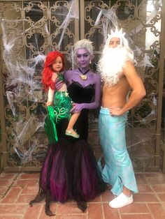 three people dressed up as mermaids pose for a photo in front of an iron gate