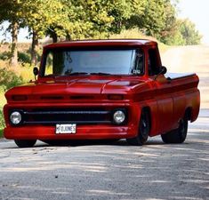 an old red pickup truck parked on the side of the road with trees in the background