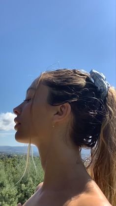 a woman with her hair in a ponytail looking out at the sky and trees on a sunny day