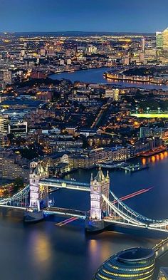 an aerial view of london at night with the tower bridge and city lights in the background