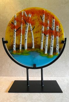 a glass plate with trees painted on the front and sides, sitting on a stand